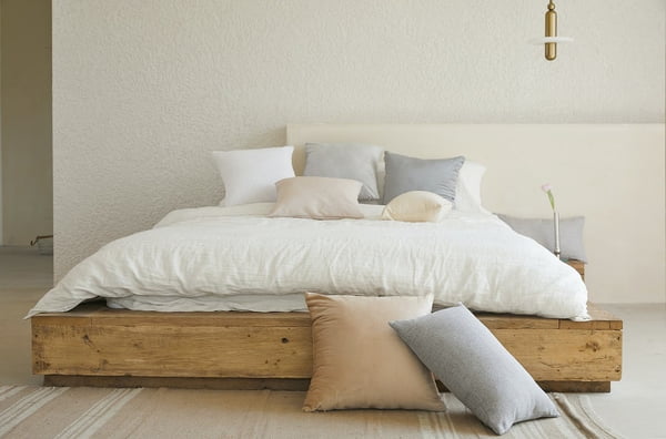 cama baixa com lençóis brancos e almofadas espalhadas