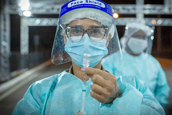 profissional de saúde com máscara e face shield segura vacina e seringa nas mãos -OPAS