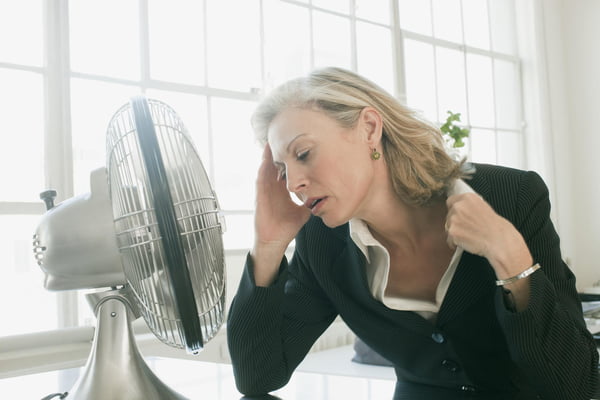 Mulher na menopausa, com calor, em frente ao ventilador - Metrópoles