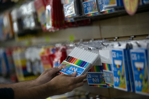 Imagem colorida mostra mão pegando embalagem com canetinhas coloridas em compra de material escolar - Metrópoles