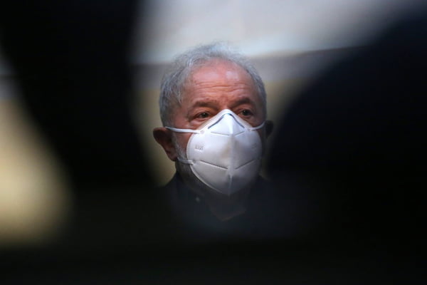 Imagem do ex-presidente Lula. Ele usa máscara e é sobreposto por objeto a sua frente - Metrópoles