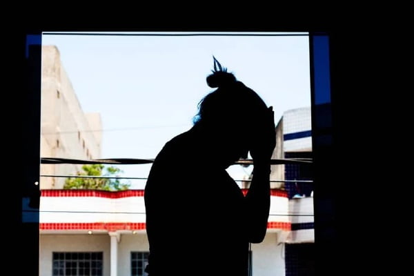 Na fotografia colorida, a mulher aparece com a cabeça abaixada e a mão na testa