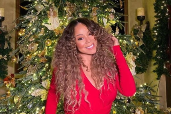 Mulher com cabelo cacheado e vestido vermelho em frente a árvore de Natal - Metrópoles