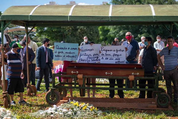 Enterro de pessoas em caixão com cartazes de protestos em cemitério