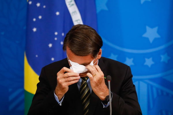 Fotografia colorida de Jair Bolsonaro retirando a máscara de proteção contra a Covid-19 - Metrópoles