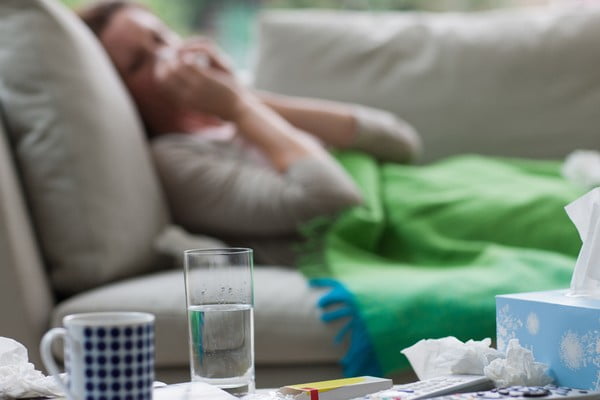 mulher doente assoa nariz em papel. Ela está deitada no sofá ao lado de medicamentos, covid longa-Metrópoles