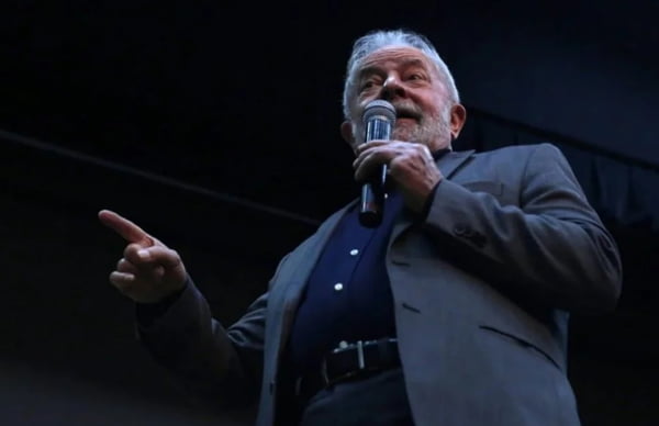 Na foto, o ex-presidente Lula (PT) é visto por baixo, usando terno e e camisa social em tons escuros, falando ao microfone e gesticulando, sem máscara - Metrópoles