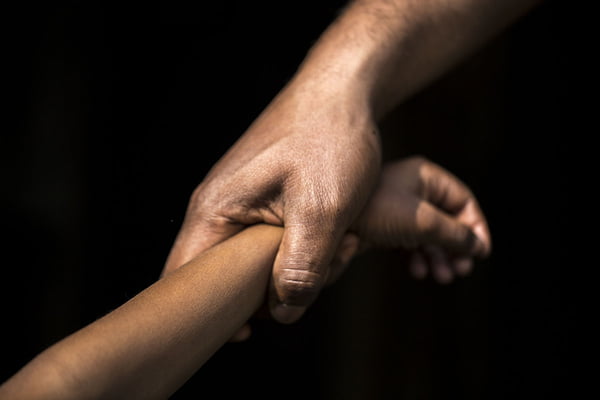 Adulto segurando o braço de uma criança em um fundo escuro