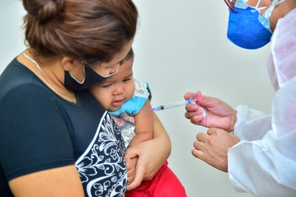Foto colorida mostra mãe com bebê durante vacinação contra a Covid - Metrópoles