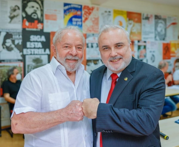 Ex-presidente Lula e o senador Jean Paul Prates, ambos do PT, posam para foto. Eles estão de frente, usam trajes sociais, e encostam os punhos num cumprimento. Ao fundo, vários cartazes de propaganda de Lula e do PT - Metrópoles