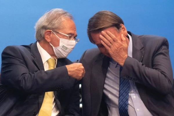 Bolsonaro e Paulo Guedes, ministro da Economia, conversam em evento no Planalto. O ministro usa máscara, o presidente não. Ambos usam terno, e Bolsonaro ri, cobrindo o rosto com a mão - Metrópoles