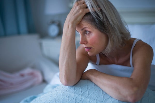 Mulher senta na cama com insônia. Ela está com a mão no cabelo-Metrópoles