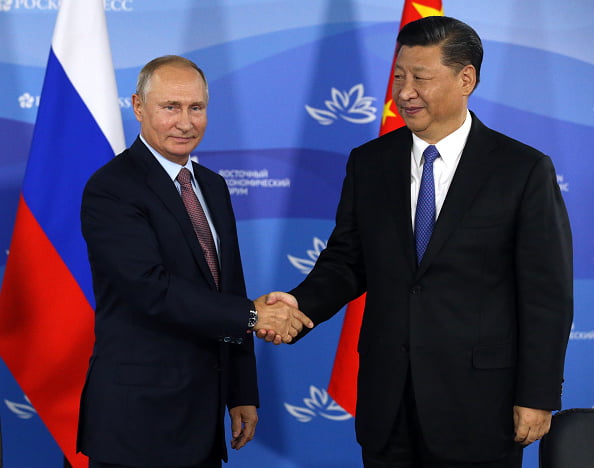Presidente russo, Vladimir Putin e o presidente da China, Xi Jinping apertam as mãos em evento. Ao fundo estão as bandeiras russa e chinesa - Metrópoles