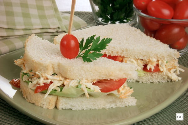 na foto vemos um sanduiche de frango e pao de forma partido na diagonal sobre um prato