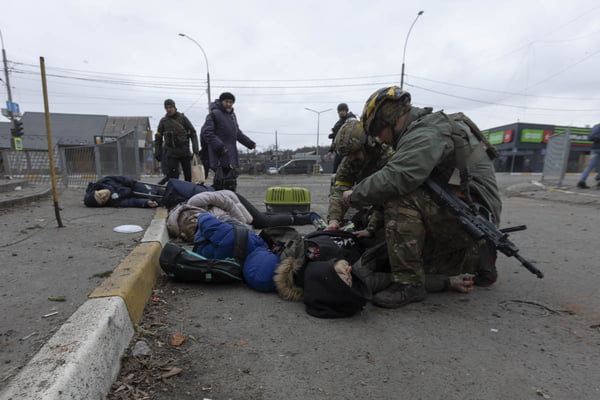 Soldados tentam salvar a vida de civíl jogado no chão após bombardeio russo. Ao lado, estirados, estão os corpos de seus familiares mortos - Metrópoles