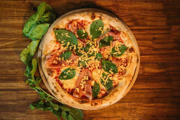 Foto de pizza com folhas verdes por cima e do lado esquerdo