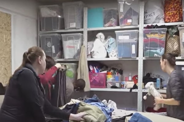Mulheres separam peças de roupas velhas em uma mesa e em caixas em uma empresa que faz reciclagem