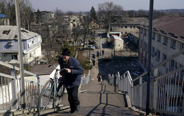 Civil sobe escadaria com sua bicicleta na cidade de Mariupol, Ucrânia, fortemente atingida por ataques russos, evacuado pelo corredor humanitário. O cenário da área residencial é de destruição - Metrópoles