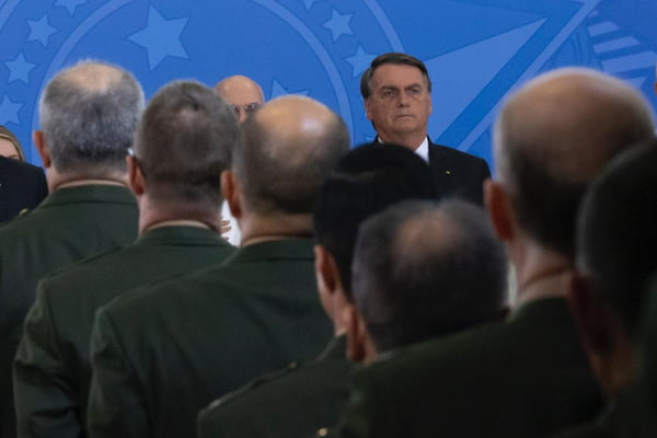 O presidente Bolsonaro cumprimenta os Oficiais-Generais promovidos na cerimônia realizada no palácio do Planalto. Ele olha os oficiais enfileirados frente ao palco com fundo azul - Metrópoles