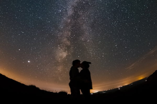 Duas pessoas se beijando com o céu estrelado atrás