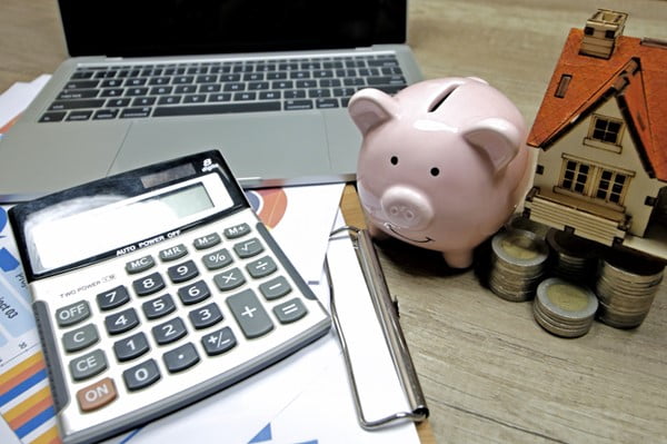 Calculadora, papeis, notebook, moedas e um cofre em formato de porco em cima de uma mesa crédito consignado - Metrópoles