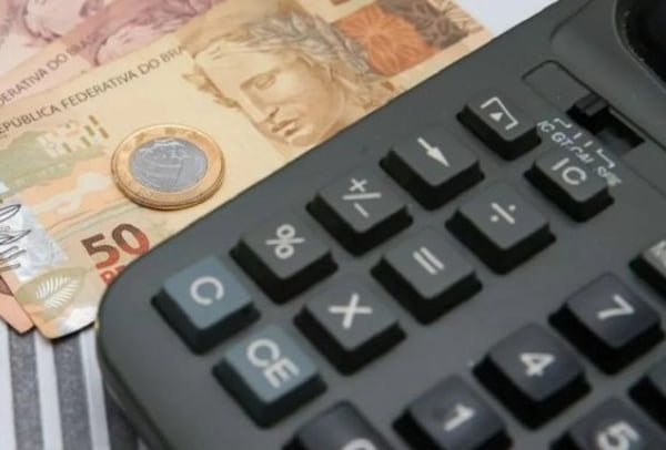 Cédulas e moedas ao lado de uma calculadora preta - Metrópoles