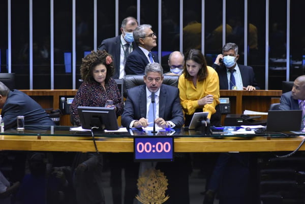 O presidente da Câmara dos Deputados, deputado Arthur Lira (PP-AL) fala ao microfone sentado em mesa diretora, cercado de assessores e deputados - Metrópoles