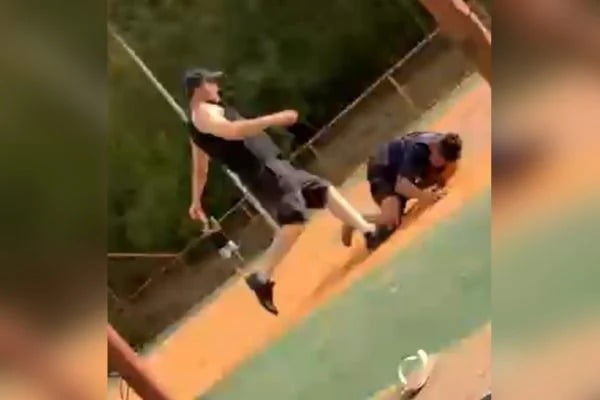 Homem de boné e roupa preta chuta menino de 14 deitado em chão de quadra poliesportiva no Núcleo Bandeirante, DF, como mostra vídeo amador - Metrópoles