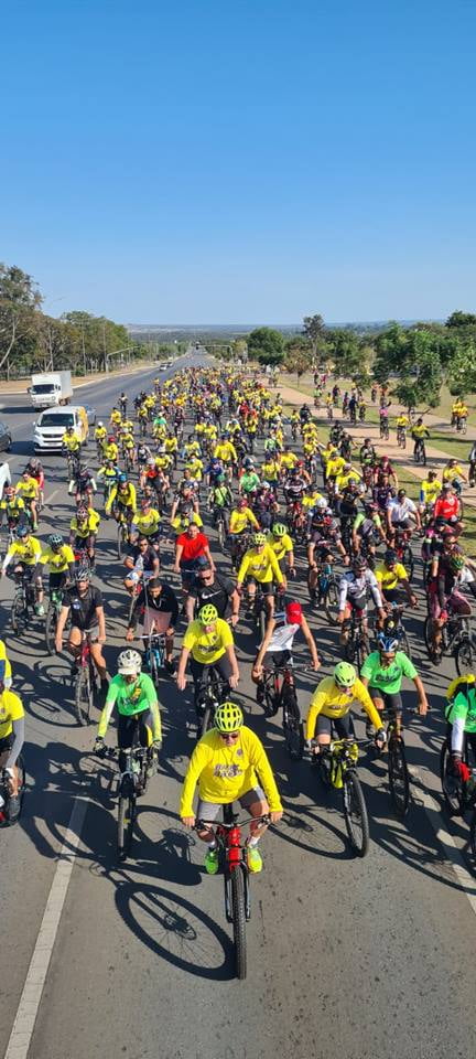 foto colorida vertical de centenas de ciclistas vestidos com roupas amarelos, verdes e vermelhas