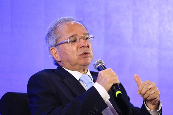 O ministro da economia, Paulo Guedes, discursa segurando um microfone. Ele usa terno e gravata - Metrópoles