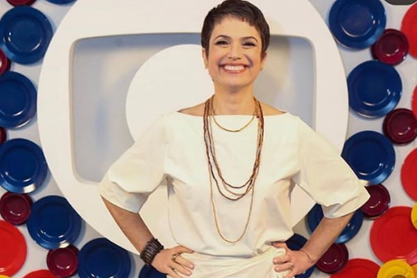 Sandra Annenberg vestida de branco em frente a uma logo da Rede Globo
