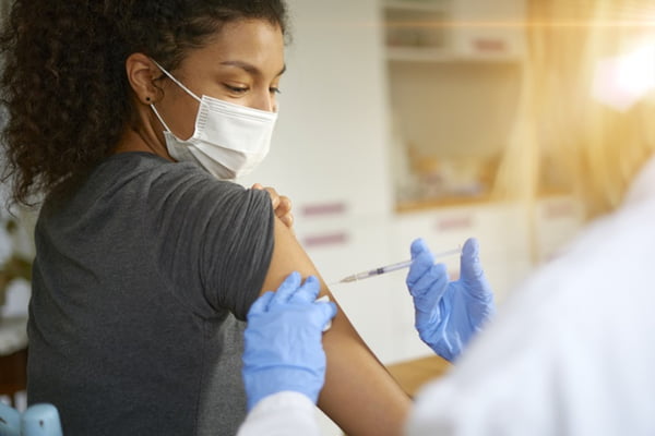 Mulher com os cabelos presos e blusa cinza sendo vacinada- Metrópoles