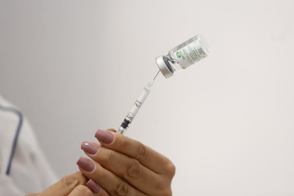Imagem de uma mão feminina segurando uma seringa e uma vacina contra a gripe - Metrópoles