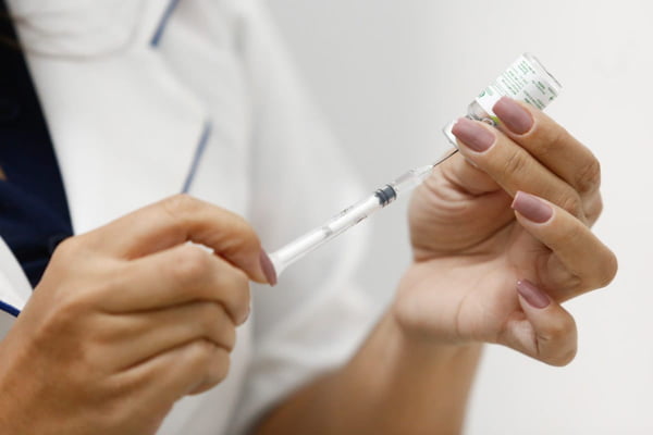 Imagem colorida da mão de uma mulher segurando uma vacina contra gripe