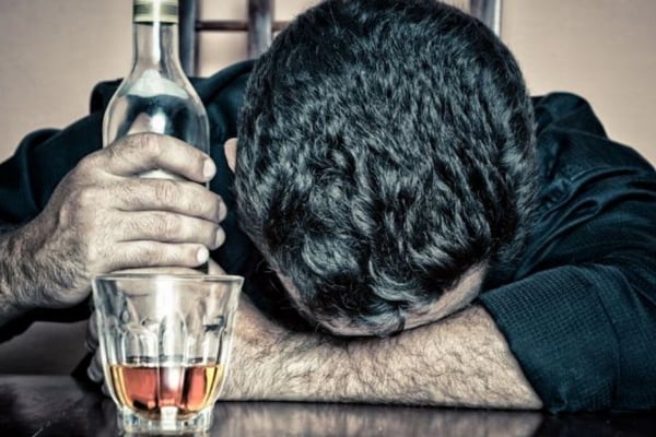 fotografia de homem com cabeça baixa segurando garrafa de bebida alcoólica