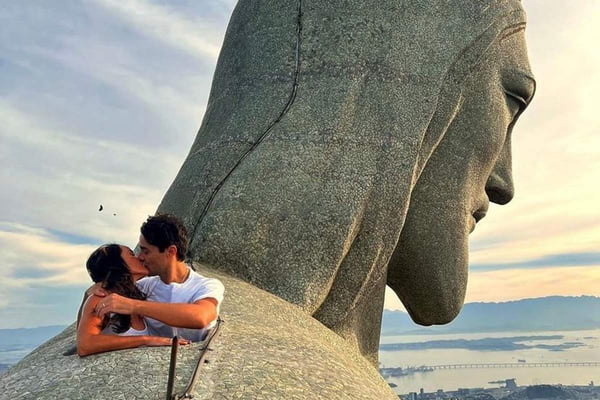 Ator Ricardo Pereira é pedido em casamento do topo do Cristo Redentor. Na foto ele beija sua esposa, dentro de um buraco na pedra do monumento e é possível ver o céu azul e mar ao fundo - Metrópoles