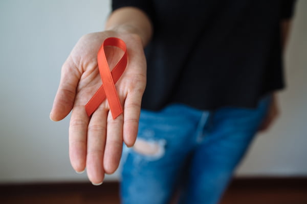 Imagem mostra fita laranja, símbolo da aids e hiv, na mão de uma pessoa - Metrópoles