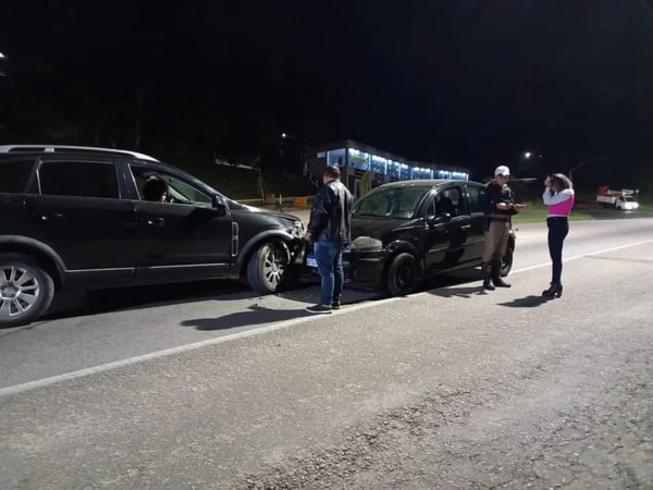 Dois carros pretos batidos em rodovia, de noite, onde motoristas observam estrago e conversam com policiais. O motorista que invadiu pista tentou se justificar - Metrópoles