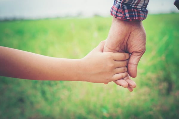 Foto ilustrativa de paternidade mostra uma criança segurando a mão de um adulto