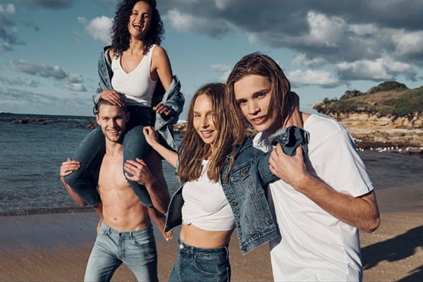 Grupo de amigos na praia usando looks com jeans