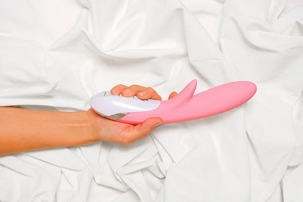 foto colorida de uma mão feminina segurando um sex toy cor de rosa em um fundo branco - Metrópoles