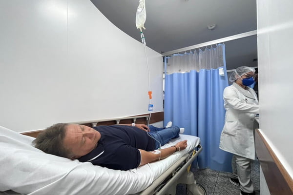 Homem de camisa preta e calça jeans descansa em maca do hospital