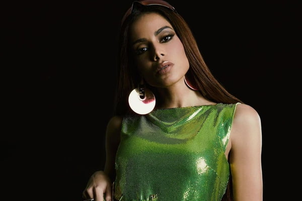 A cantora brasileira Anitta posa para foto, usando blusa de paetes verdes e brincos circulares grandes - Metrópoles