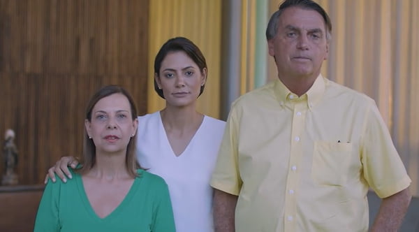 Em vídeo, Bolsonaro aparece ao lado da esposa, Michelle, e de mulher venezuelana pedindo desculpas por sua fala sobre prostituição de meninas do país. Ele usa camisa amarela e as mulheres, verde e branca - Metrópoles