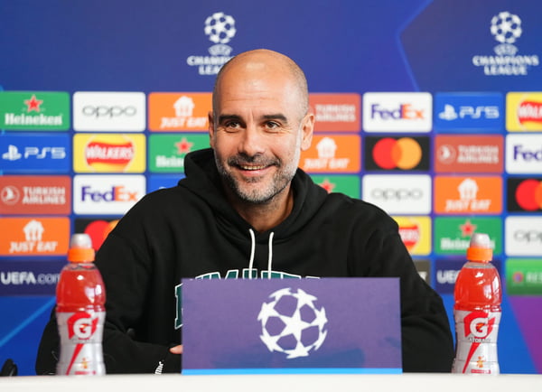 Em imagem colorida, Pep Guardiola, técnico do Manchester City, está com casaco preto falando ao microfone - Metrópoles