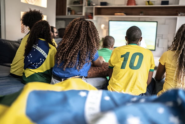 Foto colorida: grupo de amigos sentados de costas assistem jogo de futebol da seleção brasileira - Metrópoles