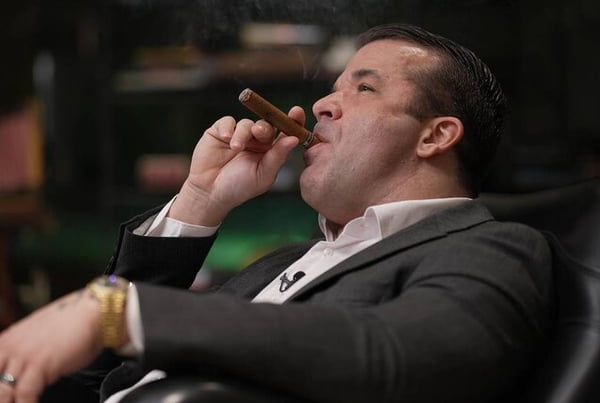 Imagem colorida do empresário Thiago Brennand fumando um charuto