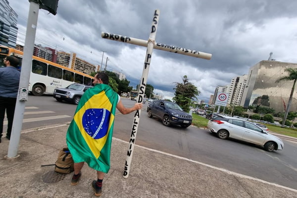 Imagem colorida de bolsonarista se manifestando na W3 Norte com cruz