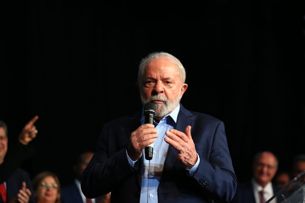O presidente eleito Lula em coletiva de impresa para anúncio de novos ministros para o próximo governo. Ele fala em púlpito diante de microfone - Metrópoles
