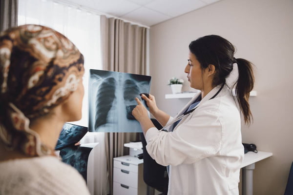 Paciente sentada na maca vê médica apresentando raio-x de seu toráx